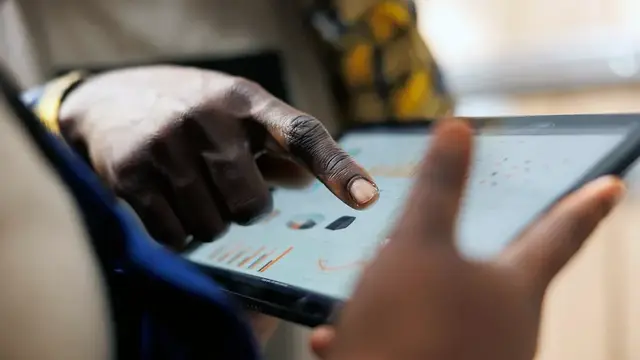 Close-up of a person pointing at charts on a tablet screen held by a colleague