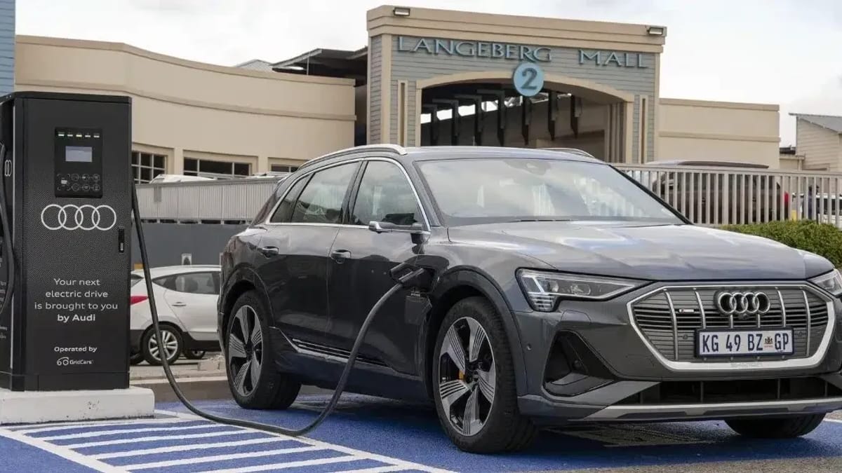 A dark grey electric SUV plugged into a public charging station outside Langeberg Mall