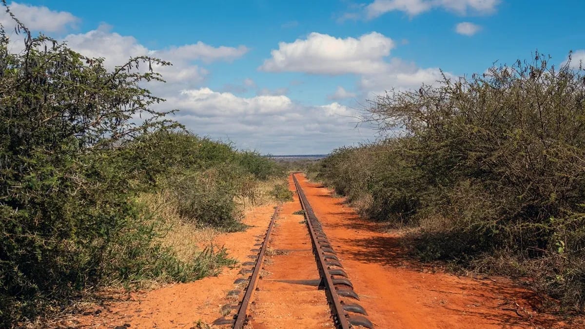 A single railway line running straight through red earth and dry bush under a blue sky