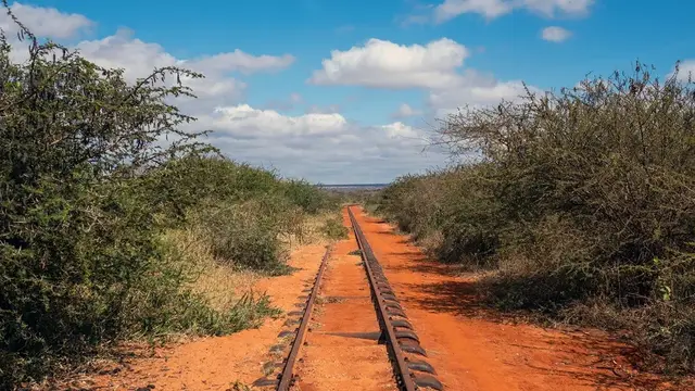 A single railway line running straight through red earth and dry bush under a blue sky