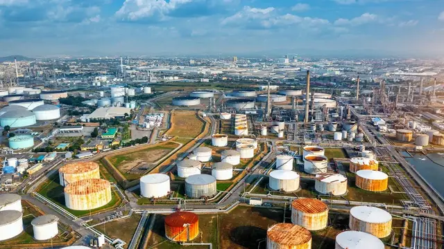 Aerial view of a large oil refinery with rows of white and rust-coloured storage tanks and pipelines