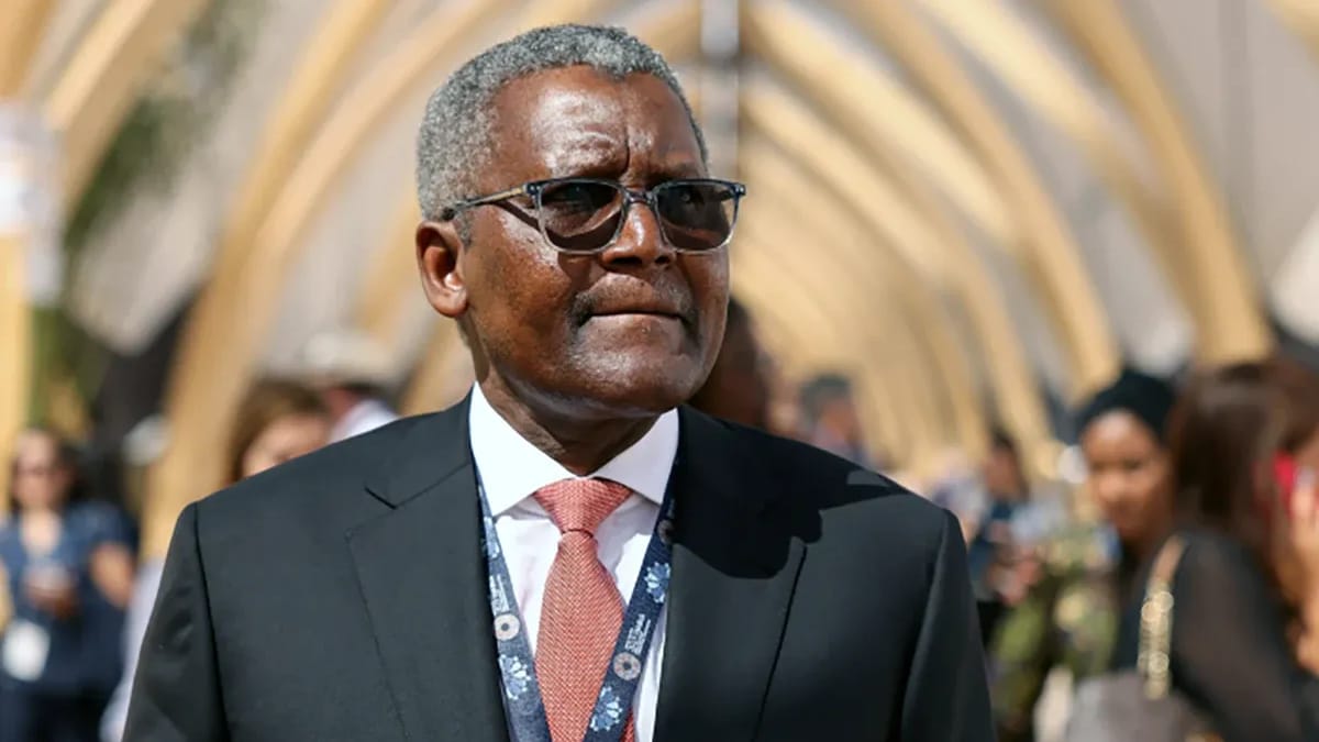 A businessman in a dark suit, red tie and event lanyard at an outdoor conference