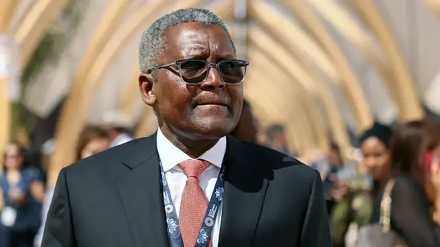 A businessman in a dark suit, red tie and event lanyard at an outdoor conference
