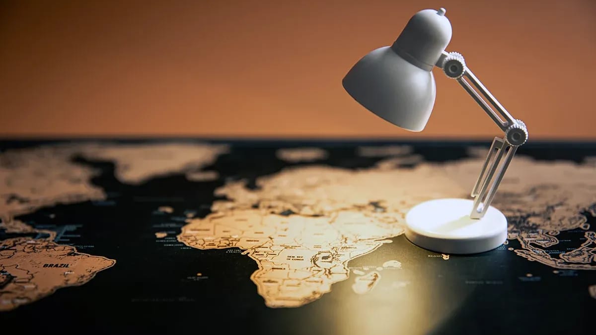 A small white desk lamp shining on the African continent on a dark scratch-off world map